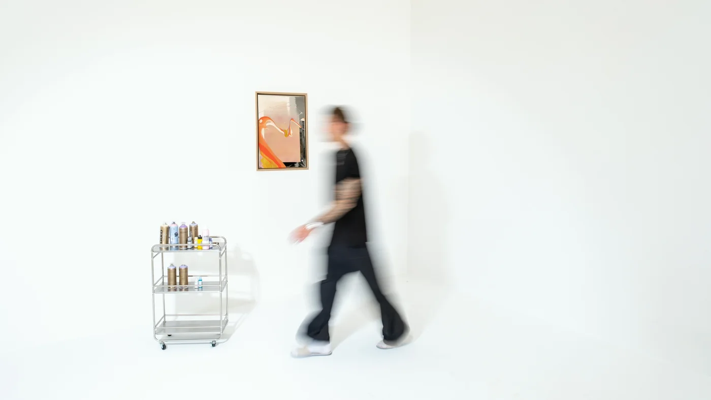 Valentin Nieroba walks past a framed WAVES OF LIFE painting in a bright white studio, next to a cart with spray cans