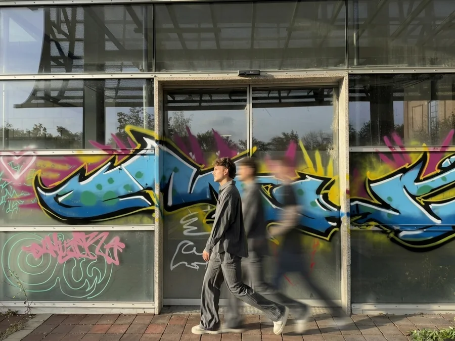 Valentin Nieroba and friends walk past a colourful graffiti mural on a glass facade